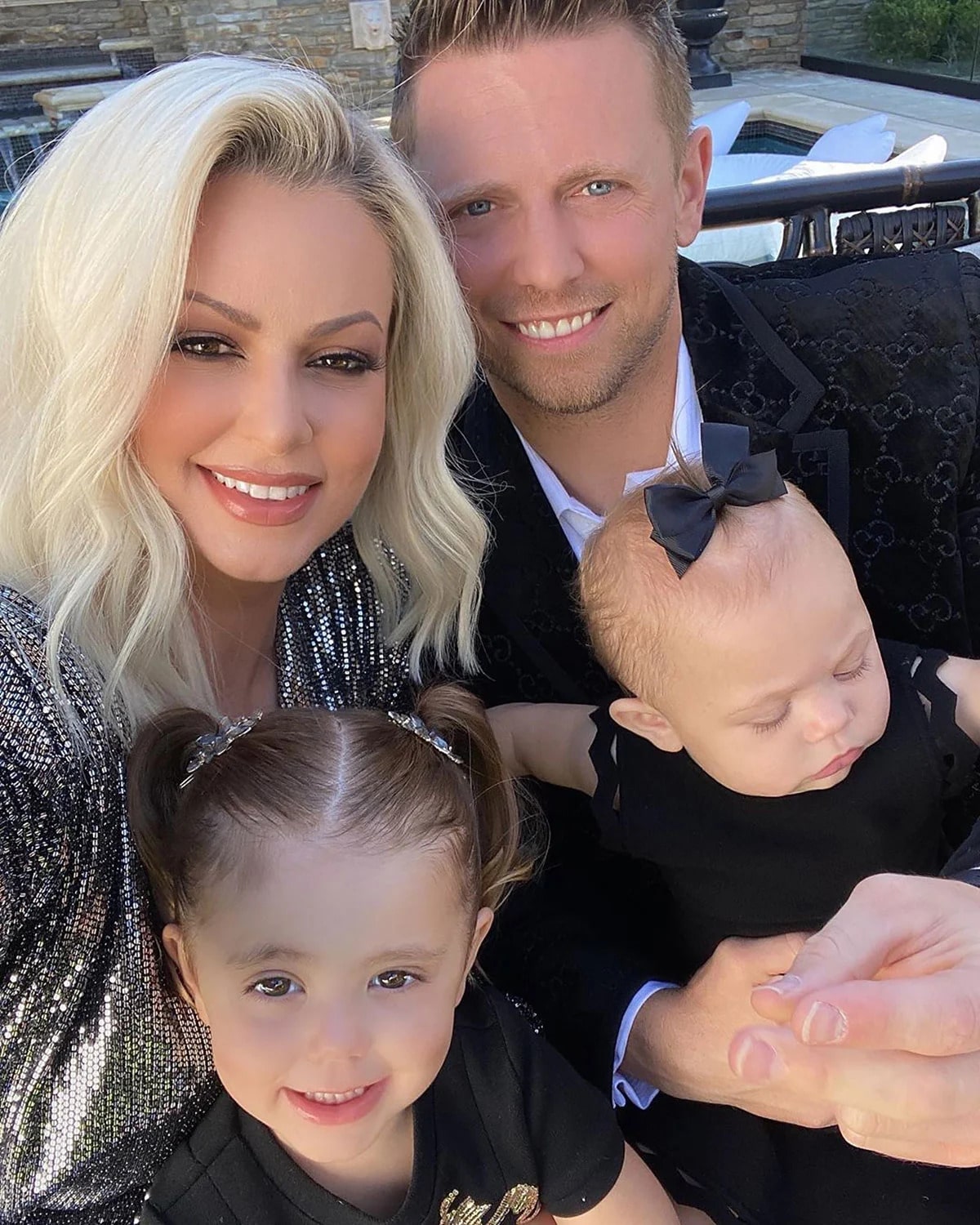 The Miz in a black velvet coat posing with his wife in a grey lined top and his children in black dresses.